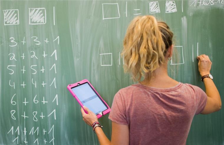 Politik einigt sich auf mehr Geld für Schulen Eine Lehrerin schreibt an eine Schultafel im Mathematikunterricht einer 8. Klasse und blickt dabei auf einen Tablet-Computer iPad.