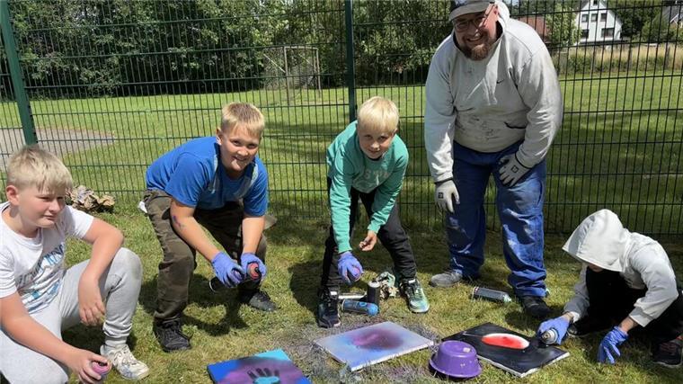 Von LoxRock bis Spacecamp: Jugendpflege Loxstedt zieht Bilanz für 2024 Kinder und ein Betreuer gestalten im Freien kreative Bilder mit Farbspraydosen; sie arbeiten auf dem Rasen vor einem Zaun, umgeben von buntem Material.