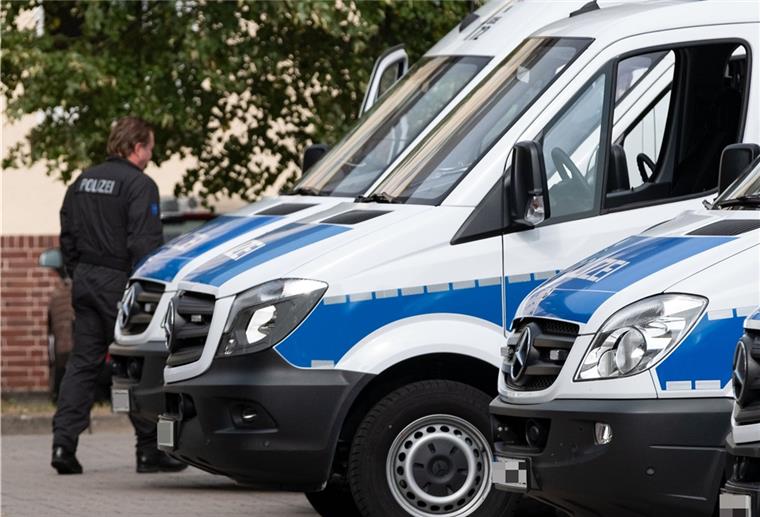 Drei Polizeiautos parken und ein Beamter läuft vorbei. 