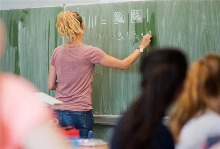 Hunderttausende Beamte sollen 5,5 Jahre länger schuften! Radikale Reform gefordert Eine junge Lehrerin schreibt an einer Schultafel.