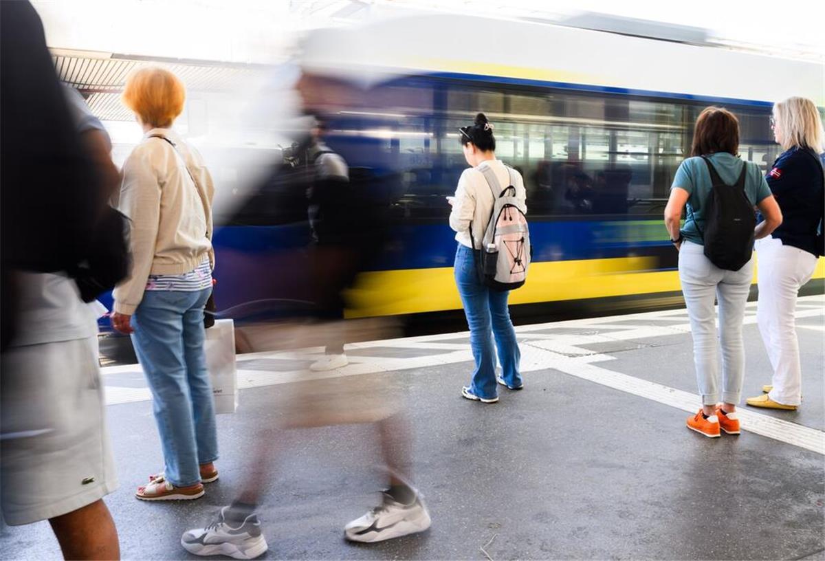 Mehrere Menschen stehen an einem Bahnhof während eine Nordwestbahn einfährt.