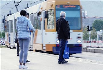 Menschen warten an einer Straßenbahnhaltestelle auf die Ankunft einer Straßenbahn. 