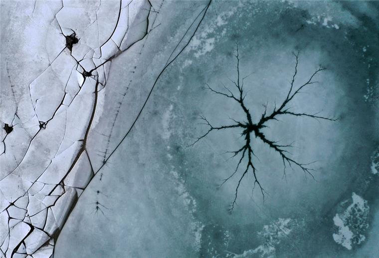Ein sternförmiger Riss ist auf der Eisfläche des Forggensees neben am Ufer liegenden gebrochenen Eisplatten zu sehen (Luftaufnahme mit einer Drohne).