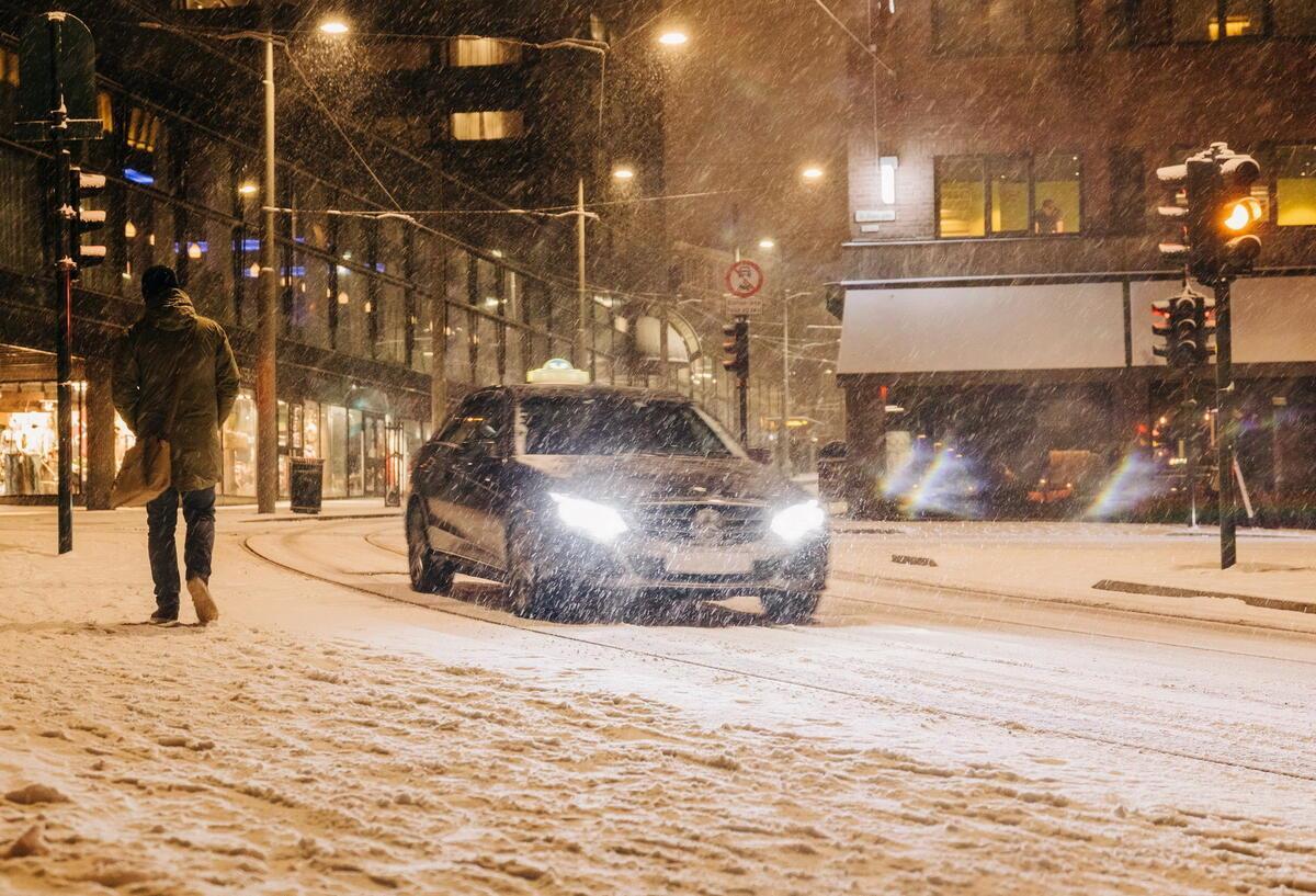 Winterreifen 2025: Das müssen Autofahrer jetzt wissen Bei Schneefall fährt ein Auto durch die Straßen. Es ist dunkel.