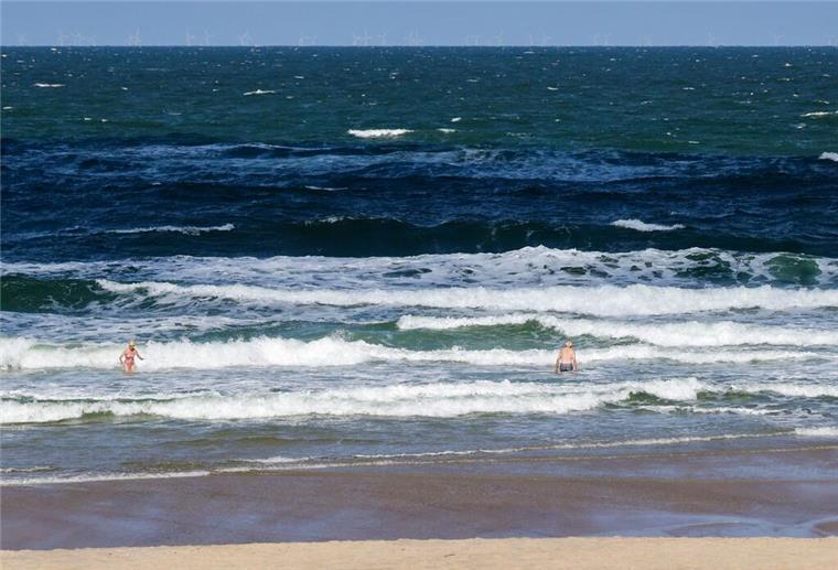 Strandbesuchende stehen bei sommerlichem Wetter in der Nordsee-Brandung am Strand in Westerland.