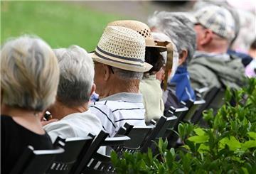  Ältere Menschen besuchen in einem Kurpark das Konzert eines Schulorchesters. 
