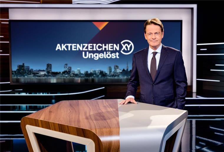 „Aktenzeichen XY...“: Neue Sendetermine mit brisanten Kriminalfällen «Aktenzeichen XY... Ungelöst»-Moderator Rudi Cerne steht im Studio und lächelt in die Kamera.