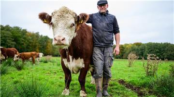 Alexander Schmidt, Rinderzüchter, steht auf einer Wiese neben dem Hereford-Rind mit dem Namen Simba.