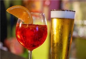 Ein Glas mit Aperol Spritz und eines mit Bier.