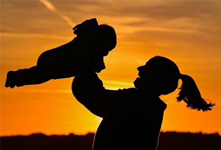Ein Mutter mit ihrem Kind vor einem Sonnenuntergang.  Alleinerziehend? In Deutschland trifft das auf deutlich mehr Mütter als Väter zu.