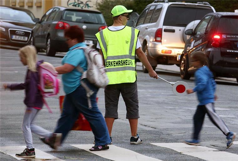  Ein Verkehrshelfer (Schülerlotse) steht an einem Fußgängerüberweg und überwacht den Schulweg der Kinder. 