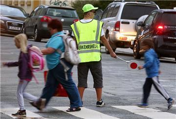  Ein Verkehrshelfer (Schülerlotse) steht an einem Fußgängerüberweg und überwacht den Schulweg der Kinder. 