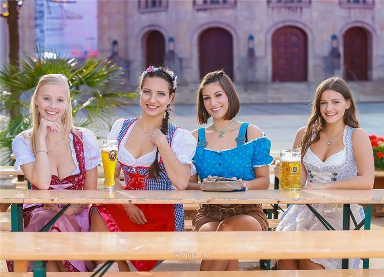 Hier findet am 15.06. das urigste Sommerfest in Bremerhaven statt! Vier junge Frauen in Trachten sitzen auf einer Bierbank.