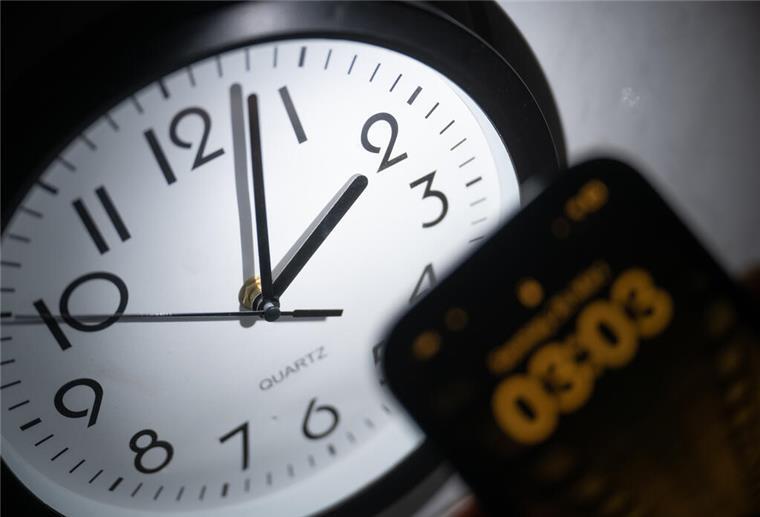 Zeitumstellung nervt die Deutschen Ein Smartphone zeigt die Uhrzeit «03:03» an, während auf einer analogen Uhr noch 02:03 Uhr ist.