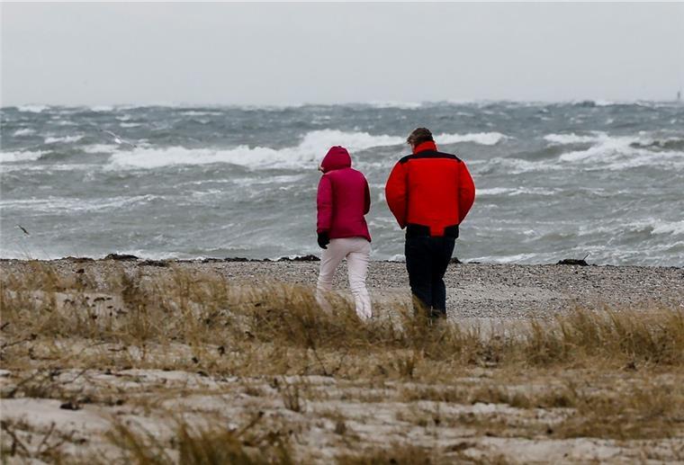 Erster Herbststurm: Im Norden stehen windige Tage an Zwei Personen gehen bei stürmischen Wetter am Strand spazieren.