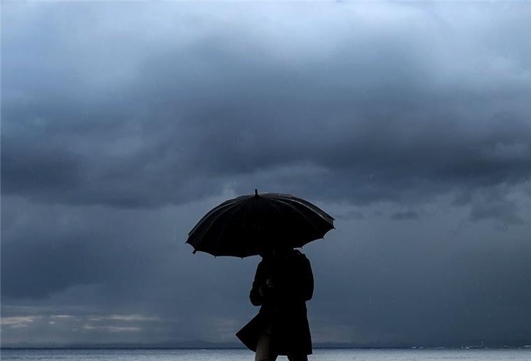 Warnung für das Küstengebiet: Sturmtief zieht über den Norden Ein Mann hält einen Regenschirm, während er am Meer entlang spazieren geht.