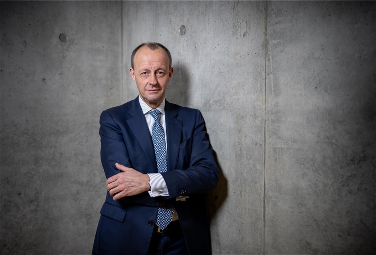Friedrich Merz mit verschränkten Armen vor einer Mauer.