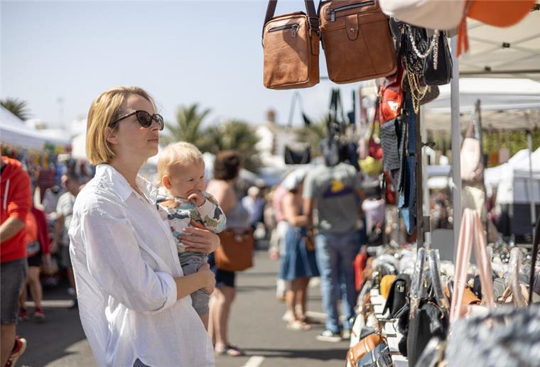 Alte Bürger lädt ein: Flohmarkt und Livemusik am 14. September Eine Frau hält ein Baby auf dem Arm und schaut sich auf einem Flohmarkt um.