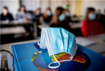 Eine OP-Maske liegt in einem Klassenzimmer auf einem Buch.