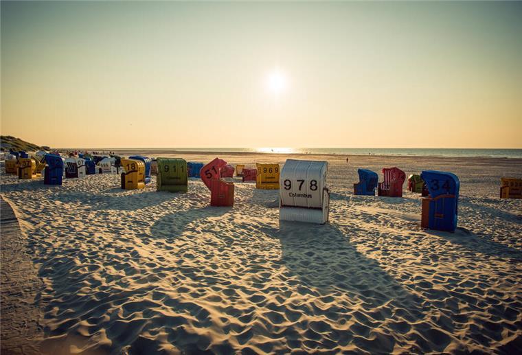 Mehrere Strandkörbe stehen am Strand und die Sonne geht unter.