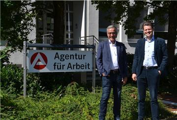 Oliver Lemke und Gregor Stein stehen neben dem Schild vor dem Eingang der Arbeitsagentur in Rotenburg