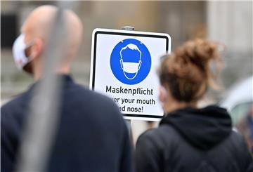 Zwei Menschen stehen vor einem Schild auf dem "Maskenpflicht" steht. 