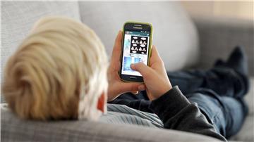 ARCHIV - Ein Kind liegt auf einem Sofa und blickt auf sein Smartphone.