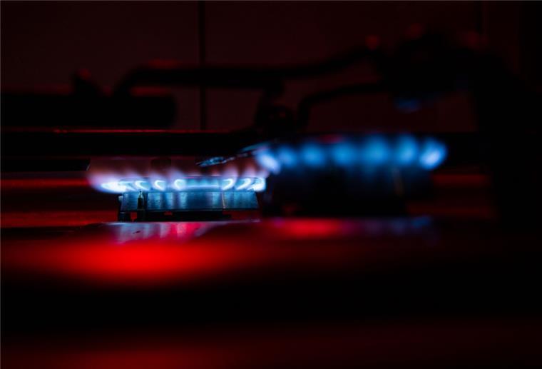Gaspreisbremse als Herkulesaufgabe: Preissenkung und Sparanreize Zwei Gasfelder auf einem Herd werden von rotem Licht angeleuchtet.