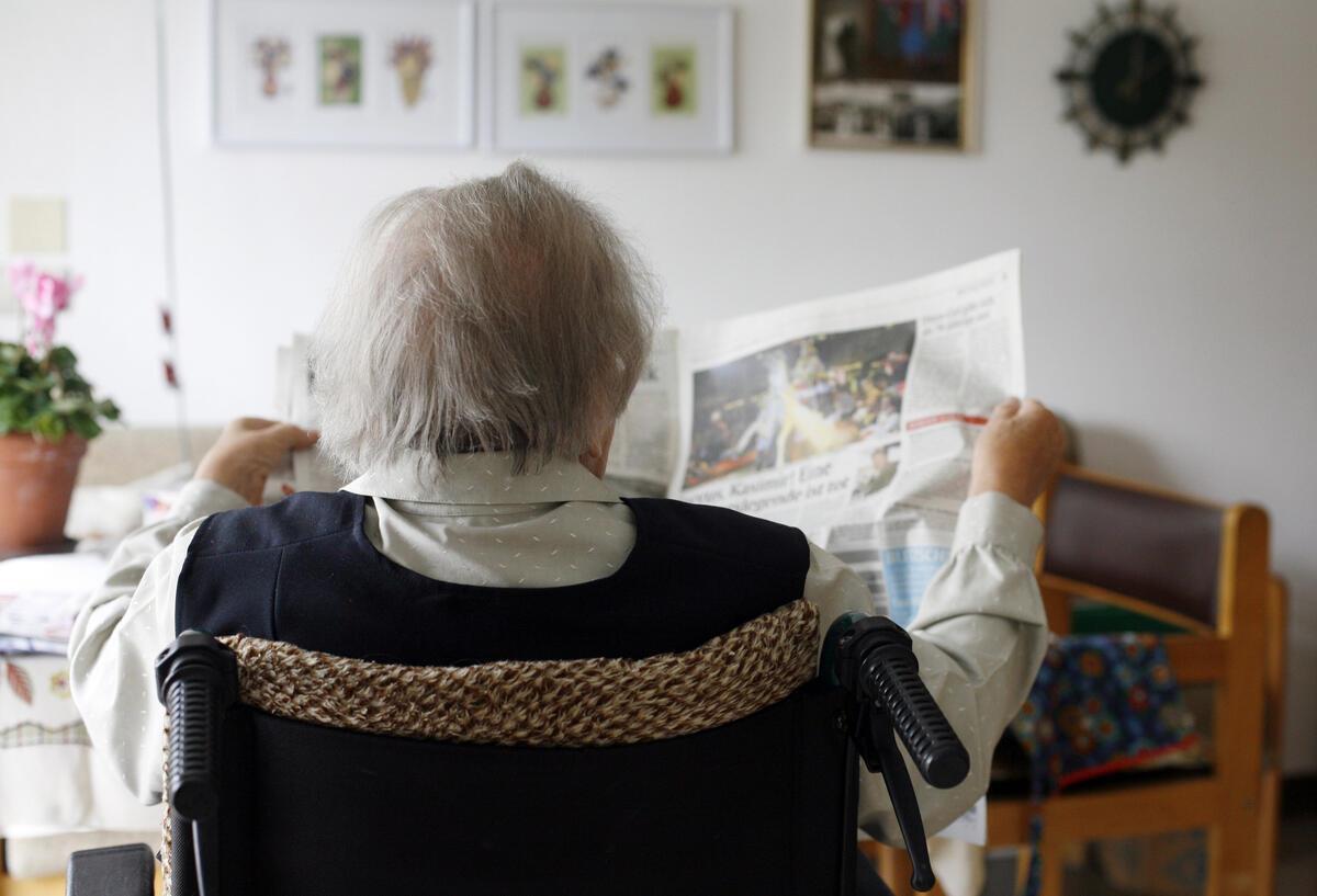Eine Seniorin sitzt im Rollstuhl und liest Zeitung.