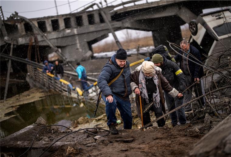 Krieg in der Ukraine: Explosionen in Kiew, Tote bei Luftangriffen Örtliche Milizionäre helfen einer alten Frau über eine von Artillerie zerstörte Brücke am Stadtrand von Kiew.