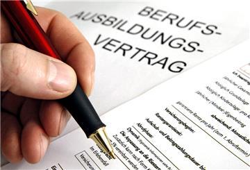 Eine Hand hält einen Stift um einen Berufsausbildungsvertrag zu unterschreiben.