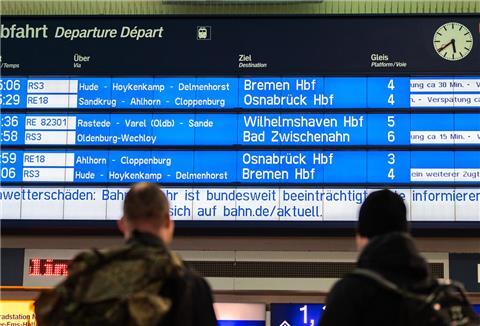 Zwei Reisende stehen am Morgen am Oldenburger Hauptbahnhof und schauen zur Anzeigetafel