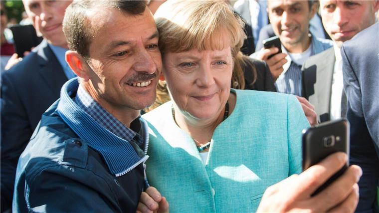 Merkel mit Geflüchteten am Tisch - zehn Jahre nach 2015 Bald zehn Jahre her: Angela Merkel (CDU) lässt sich nach dem Besuch einer Erstaufnahmeeinrichtung für Asylbewerber in Berlin-Spandau für ein Selfie zusammen mit einem Flüchtling fotografieren. (Archivbild)