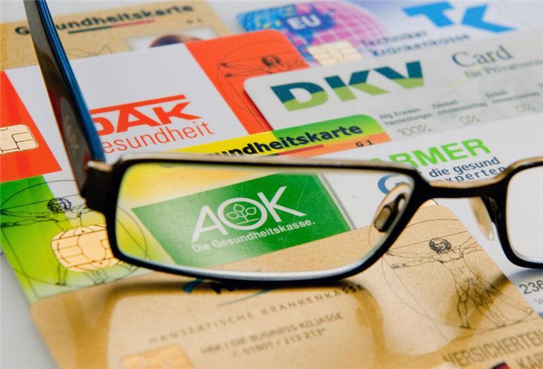 Millionen Versicherte betroffen! Harter Merz-Plan für Krankenkassen Die Chipkarten verschiedener Krankenkassen liegen unter einer Brille nebeneinander auf einem Tisch.
