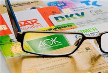 Die Chipkarten verschiedener Krankenkassen liegen unter einer Brille nebeneinander auf einem Tisch.