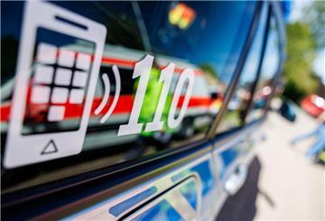 Die Nummer des Polizeinotrufs 110 steht auf der Scheibe eines Polizeifahrzeugs, in der sich ein Fahrzeug vom Roten Kreuz spiegelt.