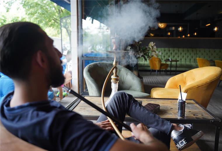 Bremer Polizei greift bei Shishabar hart durch Ein Mann sitzt in einer Bar und pustet Rauch aus. Vor ihm steht eine Shisha.