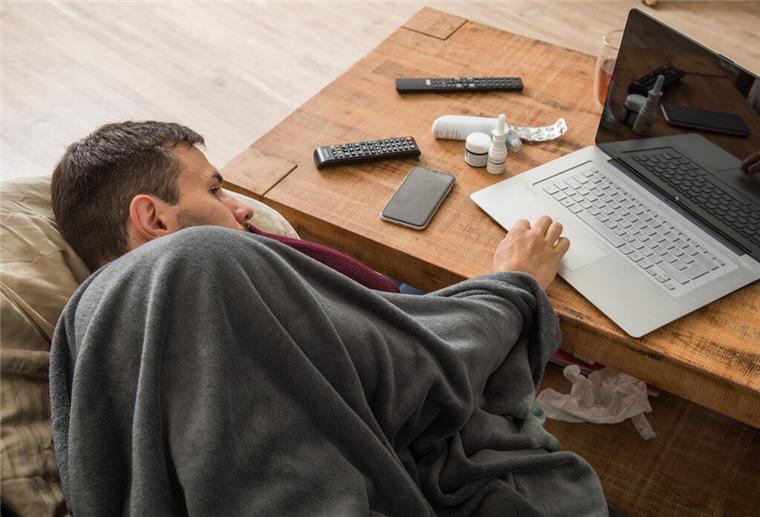 KI und Gesundheit: Warum der Chatbot den Arzt nicht ersetzen kann Ein Mann liegt angeschlagen und zugedeckt an einem Tisch, mit einer Hand bedient er einen Laptop. Bei Gesundheitsfragen kann KI helfen – doch fehlerhafte Antworten sind keine Seltenheit.
