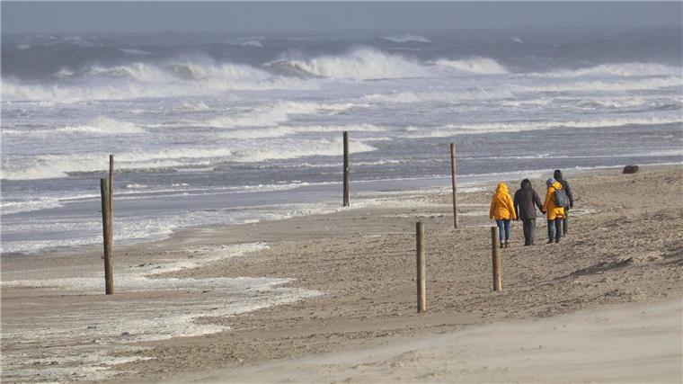 Bei stürmischem Wetter und Wellen gehen Spaziergänger am Strand entlang.