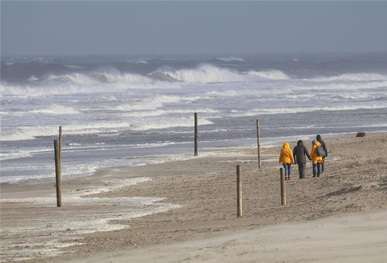 Orkanböen bis 130 km/h: Es wird stürmisch in Bremerhaven Bei stürmischem Wetter und Wellen gehen Spaziergänger am Strand entlang.
