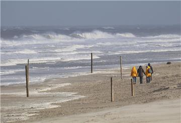 Bei stürmischem Wetter und Wellen gehen Spaziergänger am Strand entlang.