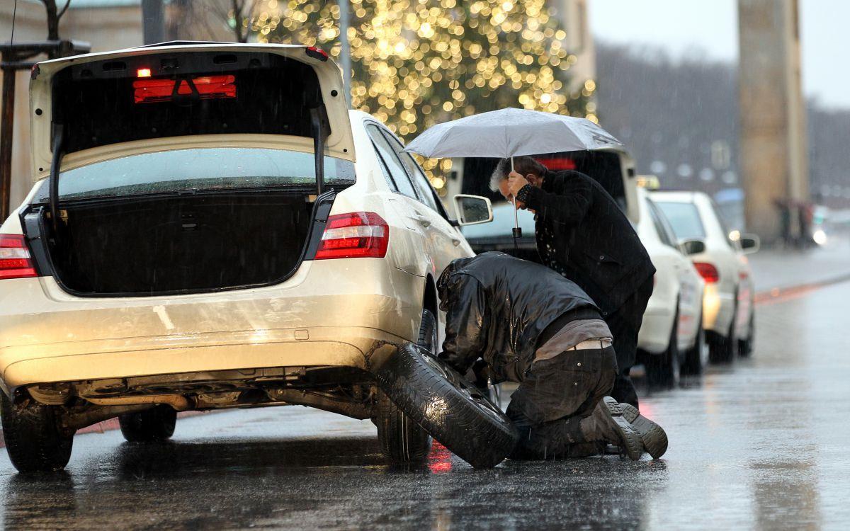 Bei Temperaturen um zwei Grad Celsius und Schneeregen muss dieser Taxifahrer einen Reifen wechseln. Ein Kollege hilft ihm, indem er einen Schirm hält. Doch eine Hilfspflicht gibt es nicht.  