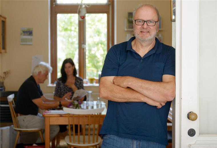 Heinfried Becker lehnt an eine Tür, im Hintergrund ein Beratungsgespräch
