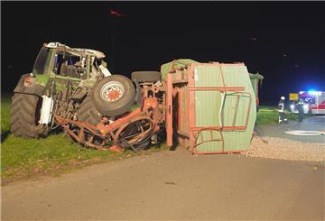 Ein Feuerwehrmann begutachtet den verdrehten Drehschemel eines landwirtschaftlichen Anhängers am zerbeulten Traktor.