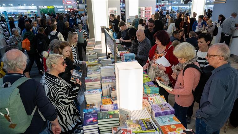 Besucherinnen und Besucher der Leipziger Buchmesse schauen sich einen Bücherstand an.