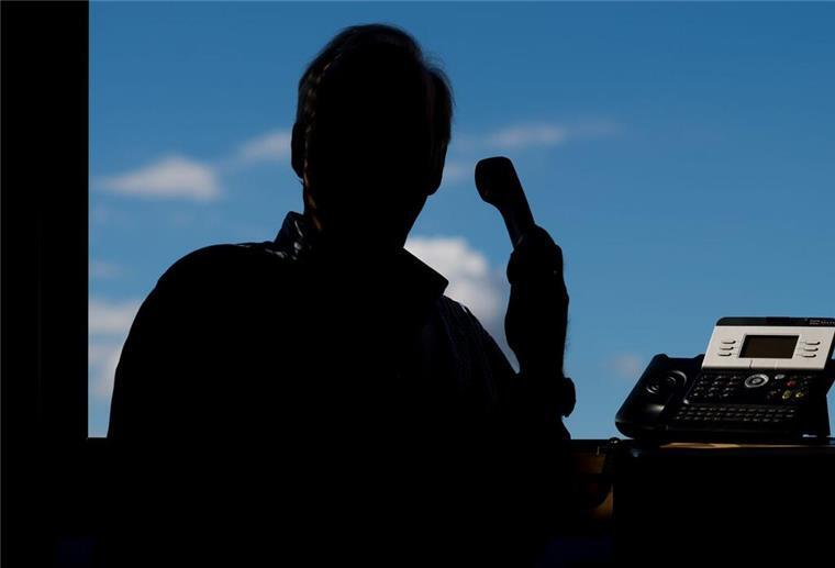 Die Silhouette eines Manns, der zum Telefonhörer greift.