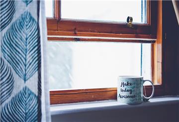 Helle Tasse, die auf einem Fensterbrett steht.