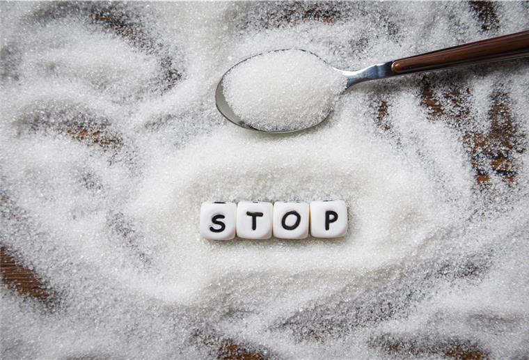 Ein Haufen Zucker verstreut auf einem Tisch. Kleine Würfel bilden das Wort "Stop". 
