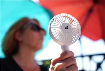 Eine Frau kühlt sich mit einem Handventilator unter Sonnenschirmen auf einem Balkon in der Mittagssonne ab
