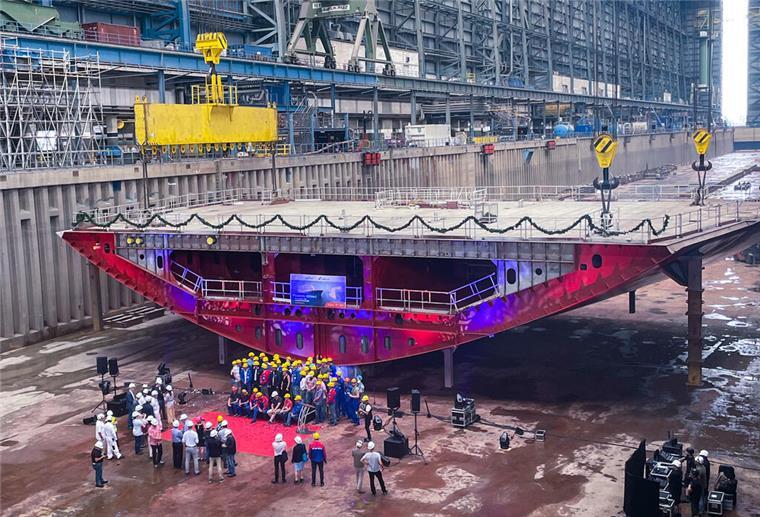 Meyer Werft legt neues Kreuzfahrtschiff für Carnival Cruise Line auf Kiel Blick in die Montagehalle der Meyer Werft: Vor einem großen roten Schiffssektionsteil der „Carnival Festivale“ stehen zahlreiche Menschen mit Schutzhelmen zu einer Feier der Kiellegung zusammen. Das Bauteil ist mit Girlanden geschmückt und von Scheinwerfern beleuchtet.